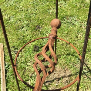 Puede incluir: Un soporte para plantas de metal oxidado con un dise&ntilde;o en espiral y una parte superior redonda. El soporte est&aacute; hecho de hierro y tiene un aspecto r&uacute;stico.