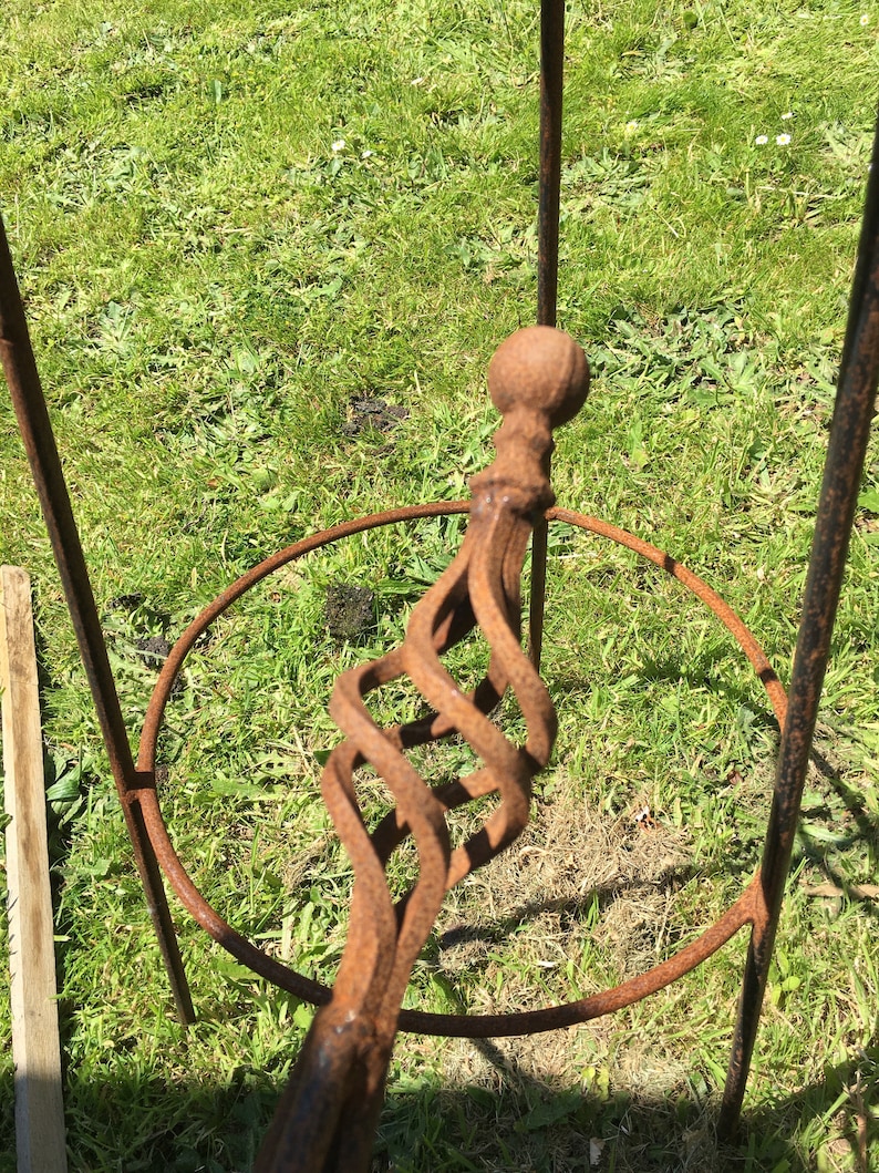 Puede incluir: Un soporte para plantas de metal oxidado con un dise&ntilde;o en espiral y una parte superior redonda. El soporte est&aacute; hecho de hierro y tiene un aspecto r&uacute;stico.