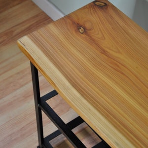 May include: A wooden bench with a live edge top and black metal legs. The bench has three shelves for storage.