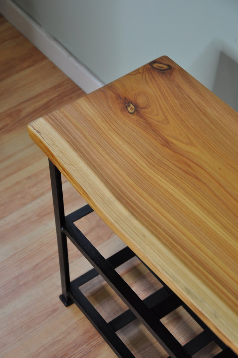 May include: A wooden bench with a live edge top and black metal legs. The bench has three shelves for storage.