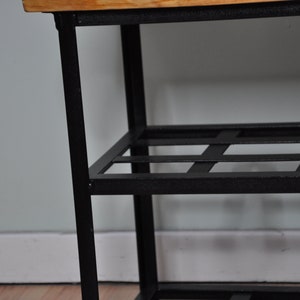 May include: A black metal shoe rack with a wooden top and three shelves. The shelves have a grid pattern.