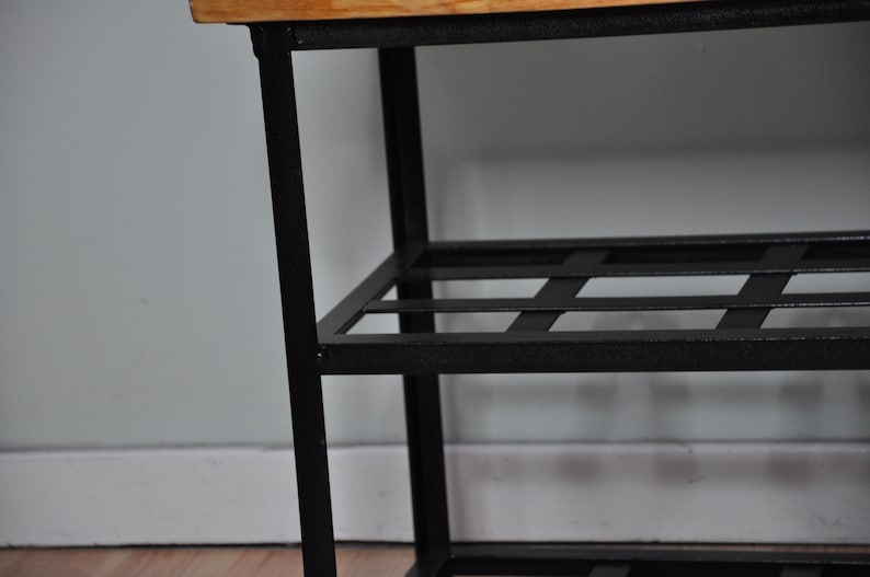 May include: A black metal shoe rack with a wooden top and three shelves. The shelves have a grid pattern.