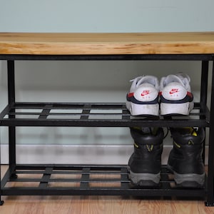 May include: A black metal shoe rack with two shelves and a wooden top. The top shelf has two pairs of white sneakers, and the bottom shelf has two pairs of black work boots.