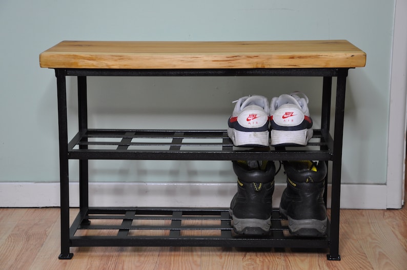 May include: A black metal shoe rack with two shelves and a wooden top. The top shelf has two pairs of white sneakers, and the bottom shelf has two pairs of black work boots.