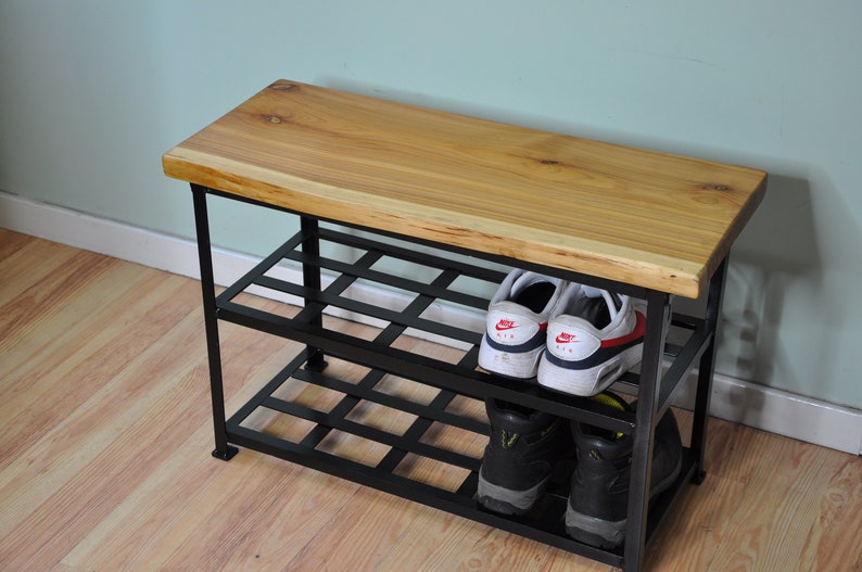 May include: A wooden bench with a metal shoe rack underneath. The bench has a live edge and the rack has two shelves. There are shoes on the shelves.
