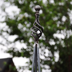 Puede incluir: Una estaca de jard&iacute;n de metal negro con un remate decorativo en forma de bola retorcida. La estaca est&aacute; hecha de tres varillas de metal que se unen en la parte superior.