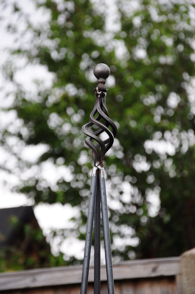 Puede incluir: Una estaca de jard&iacute;n de metal negro con un remate decorativo en forma de bola retorcida. La estaca est&aacute; hecha de tres varillas de metal que se unen en la parte superior.