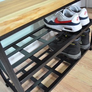 May include: A black metal shoe rack with a wooden top. The rack has three shelves and is filled with shoes. The shoes are a pair of white sneakers and a pair of black work boots.