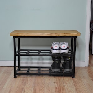 May include: A black metal shoe rack with a wooden top shelf. The rack has two shelves and is holding a pair of white sneakers and a pair of black boots.