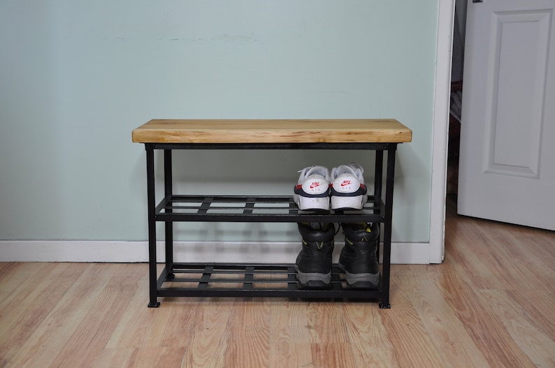 May include: A black metal shoe rack with a wooden top shelf. The rack has two shelves and is holding a pair of white sneakers and a pair of black boots.