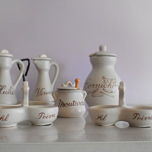 Peut inclure: Ensemble de pots à condiments en céramique blanche avec inscription brune. Les pots sont étiquetés "Huile", "Vinaigre", "Moutarde", "Cornichon", "Sel" et "Poivre".