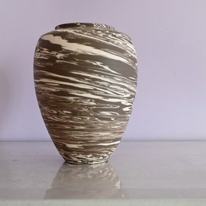 Op de afbeelding: Een bruine en witte keramische vaas met een draaiende print. De vaas is hoog en slank, met een ronde basis en een smalle opening.