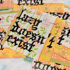 May include: Several fabric patches with the text "Lazy dreams exist" in black gothic lettering. The patches have a floral pattern with pink and green flowers on a white background, and a yellow and orange border.