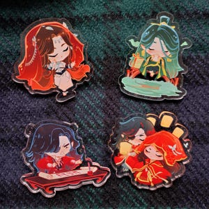 Puede incluir: Cuatro amuletos de acrílico coloridos con personajes de estilo anime. Los amuletos están en varias poses y presentan diferentes colores y diseños.