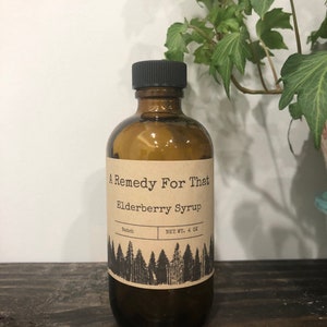 May include: A brown glass bottle with a black cap and a paper label that reads "A Remedy For That Elderberry Syrup". The label also includes the text "Batch" and "NET WT. 4 OZ".