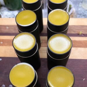 May include: A collection of cylindrical black containers with yellow tops. The containers are arranged on a wooden surface with a striped pattern. The tops have a smooth, glossy appearance, and the containers are evenly spaced.