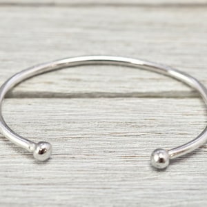 May include: A silver bangle bracelet with rounded ends. The bracelet is simple and minimalist in design.