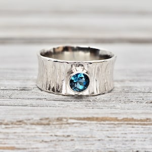 May include: A silver ring with a textured band and a blue gemstone in the centre.