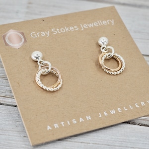 Puede incluir: Un par de pendientes de aro de plata y oro con un delicado diseño de cuentas. Los pendientes se muestran en una tarjeta que dice "Gray Stokes Jewellery Artisan Jewellery".