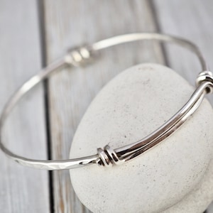 Puede incluir: Un brazalete de plata con acabado martillado y un diseño de nudo retorcido en cada extremo.