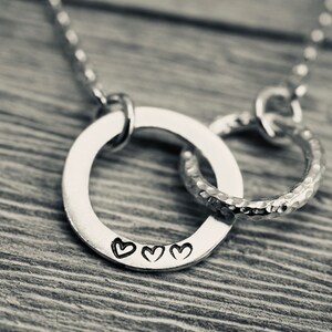 May include: A silver necklace featuring two interlocked circles. The larger circle has three small hearts engraved on it.