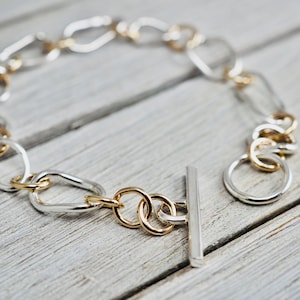 May include: A silver and gold chain bracelet with a toggle clasp. The bracelet features oval and round links.