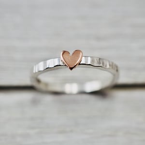 May include: A silver ring with a hammered texture and a rose gold heart charm.