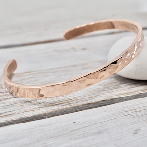 May include: A hammered rose gold cuff bracelet. The bracelet is made of a thick, flat band of metal with a hammered texture. The bracelet is open ended and adjustable.