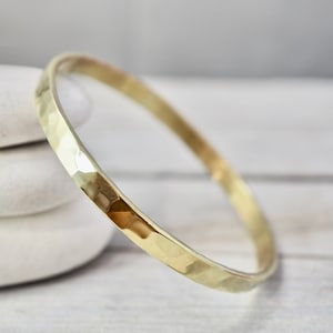 Könnte beinhalten: Ein gehämmertes Gold-Armreif-Armband. Das Armband ist aus dickem, strukturiertem Metall gefertigt und hat ein schlichtes, elegantes Design.