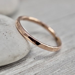 May include: A hammered rose gold band ring. The ring is thin and has a textured surface.