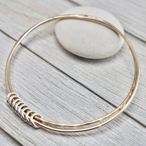 May include: A gold bangle bracelet with a silver ring detail. The bracelet is made of two thin wires that are intertwined.