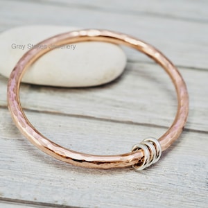 May include: A hammered rose gold bangle bracelet with a silver ring accent. Gray Stokes Jewellery.