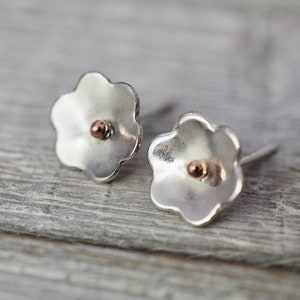 Puede incluir: Un par de pendientes de plata en forma de flor con un pequeño punto de oro rosa en el centro de cada flor.