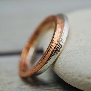 May include: Two intertwined rings, one with a copper finish and the other with a silver finish. Both rings have a textured surface.