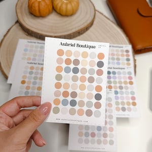 May include: A white rectangular sticker sheet featuring a grid of small solid circles in various muted earth tones, including beige, tan, grey, and soft blue. The text Aubriel Boutique and AB1011 09 are printed at the top, with a website URL at the bottom.