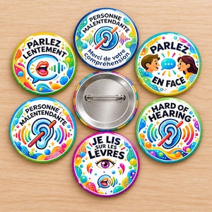 Op de afbeelding: Een verzameling van zes ronde buttons met kleurrijke grafische ontwerpen en tekst. De buttons tonen zinnen zoals Parlez Lentement, Personne Malentendante, Parlez En Face, Hard of Hearing en Je Lis Sur Les Levres.