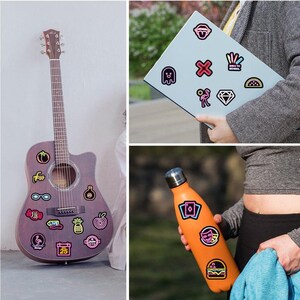 May include: A brown acoustic guitar with various colorful stickers on the body, including a pineapple, a watermelon, a pair of sunglasses, a tomato, a candy cane, a bottle, a calendar, a heart, and the word "LIVE".
