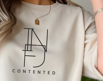 Pode incluir: Uma camisola de cor creme cortada com um design gráfico preto de uma letra estilizada "N" e a palavra "CONTENTED" impressa abaixo.