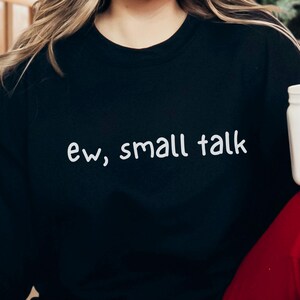 May include: Black sweatshirt with the text "ew, small talk" in white script. A white jar is visible on the right side of the image. The sweatshirt is a casual style.