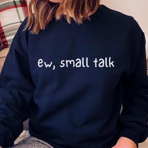 May include: Navy blue sweatshirt with the phrase "ew, small talk" in white, sans-serif font. The long-sleeved top is made of a soft material. The sweatshirt is a casual garment.