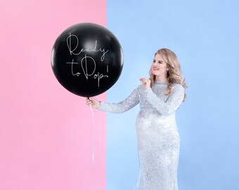 May include: A pregnant person in a silver sequined dress holds a large black balloon with the text "Ready to Pop!" written in white. The background is split in half, with pink on the left and blue on the right.