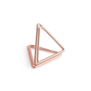 May include: A rose gold metal triangle stand with three layers. The stand is made of thin metal and is designed to hold small items.