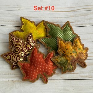 May include: A set of five fabric leaf ornaments labeled Set #10. The collection includes a yellow leaf, a green leaf with white polka dots, a gold leaf with a dark brown swirl pattern, a red leaf with white polka dots, and a mottled yellow and green leaf.