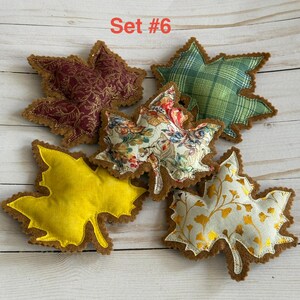 May include: A set of five fabric leaf ornaments labeled Set #6. The collection includes a solid yellow leaf, a maroon leaf with gold filigree, a green plaid leaf, a white leaf with a colorful floral pattern, and a white leaf with gold ginkgo prints.