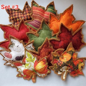 May include: A collection of fabric leaf-shaped ornaments labeled Set #3. The leaves feature various patterns including pumpkins, houndstooth, stripes, and solid autumn colors like orange, red, and green, all finished with brown scalloped edges.
