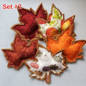 May include: A collection of five fabric leaf-shaped ornaments with scalloped felt edges. The set includes solid orange, deep red, and patterned fabrics featuring pumpkins and vines. The text Set #2 is printed in red in the upper left corner.