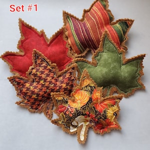 May include: A set of five fabric maple leaf ornaments labeled Set #1. The leaves feature various patterns including solid red, green, striped, houndstooth, and a pumpkin print. Each leaf has a brown felt backing with decorative pinked edges.