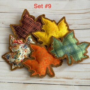 May include: A set of five fabric leaf-shaped ornaments labeled Set #9. The leaves feature various patterns including a black and orange grid, solid yellow, green plaid, orange floral, and a multi-colored autumn floral print on a cream background.