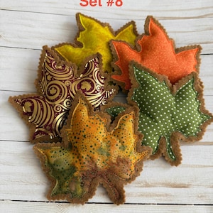 May include: A collection of five fabric leaf-shaped ornaments labeled Set #8. The leaves feature various patterns including gold swirls on burgundy, green with white polka dots, solid orange, solid yellow, and a mottled yellow-green-orange print.