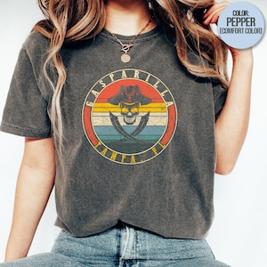 May include: Dark gray t-shirt featuring a circular graphic with a pirate skull wearing a hat, crossed swords, and the text "GASPIRILLA TAMPA FL" in a retro design. The shirt is a comfort color.